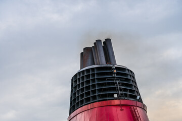 Close up of ship funnel releasing smoke into cloudy sky.