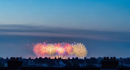 Festive fireworks explode over silhouetted townhouses in hazy sky, celebration and community.