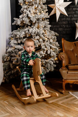 The boy is sitting in pajamas near the Christmas tree on a cart horse