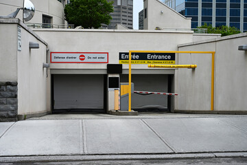 Bilingual underground parking entrance with clearance bar, concrete walls, and traffic signage in a modern urban environment. Clean, symmetrical city infrastructure in a downtown setting.