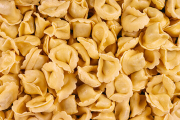 Close-up of raw yellow tortellini pasta in a full-frame composition. Fresh and uncooked, this Italian food background highlights texture and shape, ideal for culinary design and advertising.