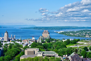 Panoramic summer view of Old Quebec with Ch&acirc;teau Frontenac, St. Lawrence River, and lush greenery under a blue sky. Iconic Canadian cityscape perfect for travel and editorial content.