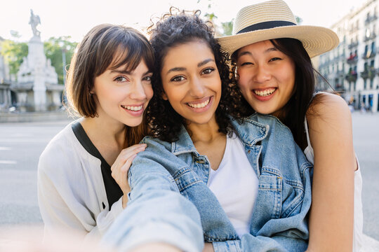 Multiracial young women taking selfie together outdoors. Smiling female friends enjoying sunny day and friendship in the city. Lifestyle and togetherness concept.