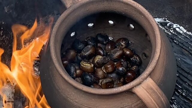 Cooking roasted chestnuts in the clay pot on fire. Fall season, homemade traditional food concept.