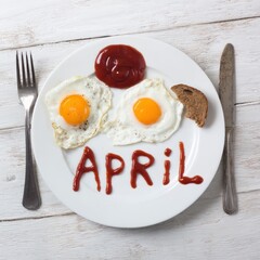 Breakfast eggs plate with ketchup text april and utensils top view