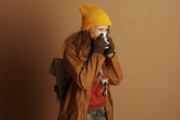 Dressed for autumn with yellow beanie and green gloves, woman gently blows nose with tissue. Her...