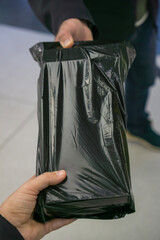 Close-up of two people exchanging a black plastic-wrapped package, symbolizing delivery, confidential transaction, or secretive exchange concept.