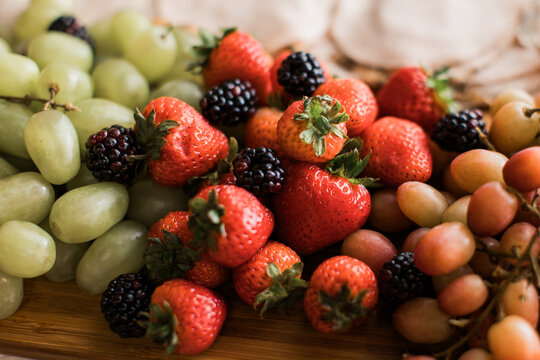 Closeup of berries, strawberries, red and green grapes, blackberries and raspberries on a wooden tray 