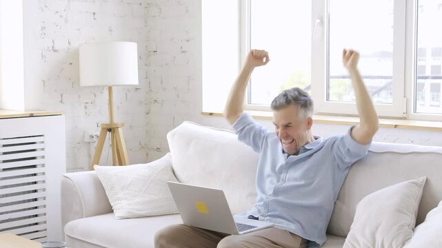 Happy mature man celebrating online success or business success using laptop 