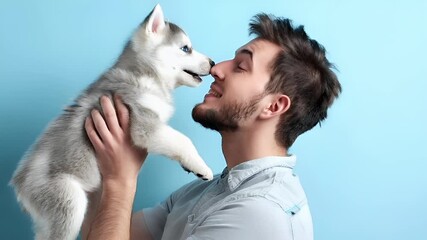 A man and a husky puppy share a tender moment against a blue background. The man is holding the puppy close to his face, with both eyes closed, suggesting a deep connection between them.