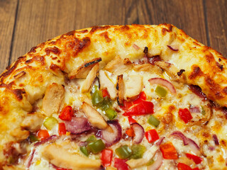 A cooked pizza with a lot of toppings including chicken, peppers, and onions. The pizza is sitting on a wooden table. Fine Italian style meal popular world wide. Rich dough base.