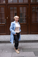 A blonde woman in a white sweater and scarf stands outside a business building. The architecture of the building is dominated by red brick.