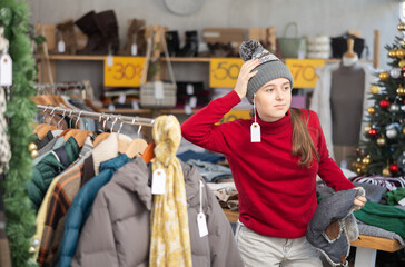 Teenage girl chooses a warm hat in a fashion boutique.