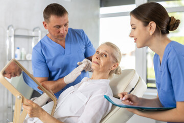 Fototapeta premium Beautician talking with patient before injection treatment, while client observing herself in mirror.