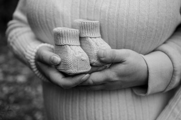 Monochrome shot: a pregnant woman's hands gently embrace her belly. A symbol of motherhood, anticipation, tenderness, and boundless love for her unborn baby