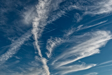 Vom H&ouml;henwind durchk&auml;mmte, wei&szlig;e, filigrane Strukturen von Schleiherwolken (Cirrostratus) mit Kondensstreifen von Flugzeugen vor blauem Himmelshintergrund
