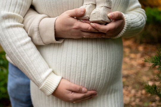 Close-up of an expectant couple's hands: the mother embraces her pregnant belly, while the father gently holds a pair of tiny knitted baby booties