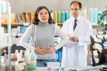Obraz premium Young woman suffering from stomach pain. Male pharmacist offering stomach pain pills