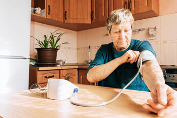 An elderly woman measures her blood pressure in the kitchen. Health maintenance, healthy aging, disease prevention, cardiovascular system monitoring, home treatment