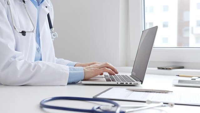 Doctor woman is typing on a laptop with a stethoscope, medical record, and pen on the desk in a bright medical office, showcasing healthcare technology and medical documentation. Medicine concept