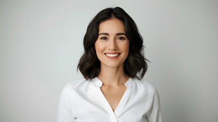 Clean professional studio portrait of a young woman in a white shirt smiling warmly against a soft neutral background, conveying confidence, approachability, modern elegance, and polished contemporary