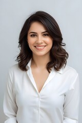 Obraz premium Clean professional studio portrait of a young woman in a white shirt smiling warmly against a soft neutral background, conveying confidence, approachability, modern elegance, and polished contemporary