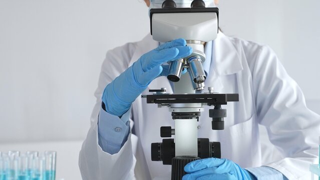 Female scientist wearing protective gear carefully adjusting microscope lens, analyzing medical research samples with precision in sterile laboratory environment
