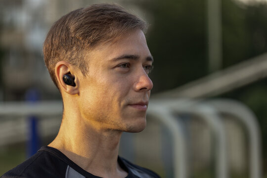 focused male athlete wearing headphones stands on a sports ground getting ready for training. He appears engaged in his workout routine as he enjoys music.