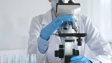 A scientist in protective gear adjusts a microscope lens and accurately analyzes medical research...