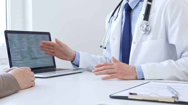 Close-up of a doctor reviewing digital test results with patient, discussing health findings on laptop screen during clinical consultation. Medicine and health care concept