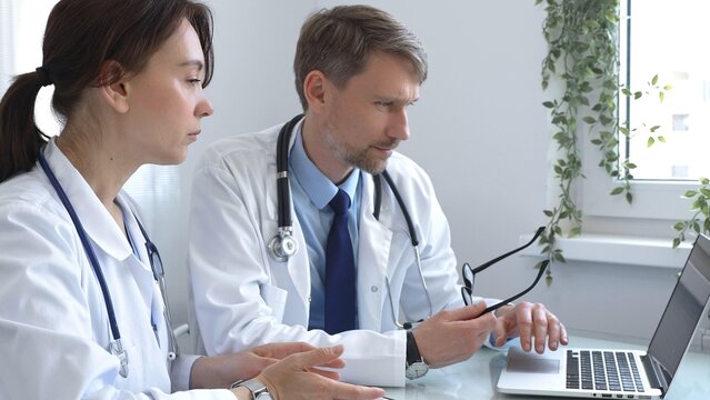 Two doctors are studying medical charts on a laptop, discussing patient data in a hospital or clinical setting. Medicine and healthcare concept.