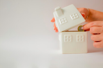 Hand dropping coin into a house-shaped piggy bank representing savings and investment