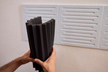 Closeup of foam insulation method, Hand pressing textured acoustic foam onto wall surface, Detailed shot of fingers securing black foam panels on gray wall Comparison of different foam rubber and
