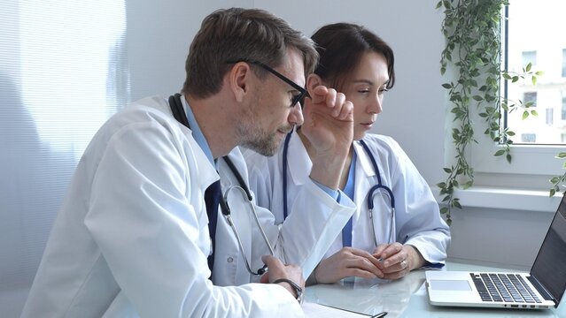 Two doctors are studying medical charts on a laptop, discussing patient data in a hospital or clinical setting. Medicine and healthcare concept. - Powered by Adobe