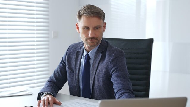 Focused mature businessman wearing suit and tie sitting at office desk and signing documents, using calculator. Audit and taxes theme in business