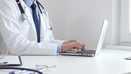Male doctor is typing on laptop, updating electronic patient records with focused concentration,...