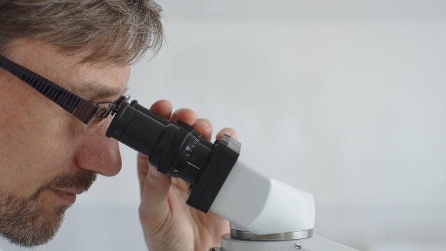 Close up of a male scientist looking through a microscope, conducting research and analysis in a laboratory setting, showcasing scientific investigation and discovery. Medicine and science concept