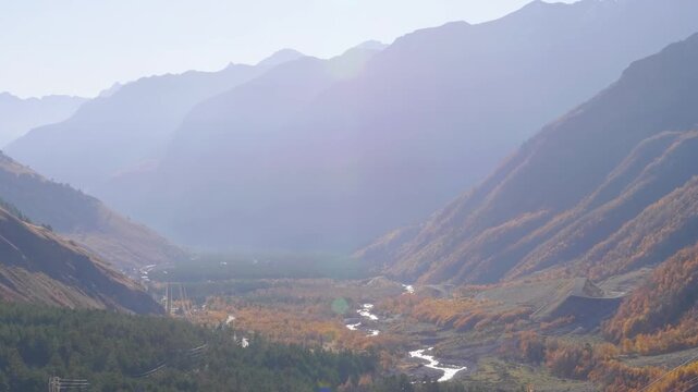 panoramic footage capturing the stunning natural beauty of a mountain valley in the North Caucasus region of Russia during the autumn season. The scene features a winding river, forested slopes covere