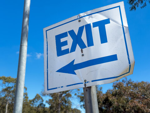 A damaged metal exit sign stands out boldly against the clear blue sky