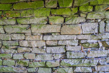 Close-up view of an aged, weathered stone village wall with moss and crevices. a