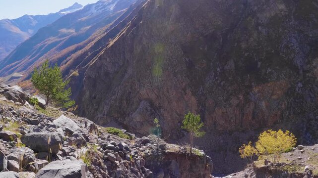 footage of a rugged mountain landscape in the North Caucasus region of Russia. The scene features rocky terrain, scattered trees, and a dramatic slope under a clear sky, capturing the raw, natural bea
