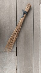 Traditional Indonesian broom made from dried coconut leaves placed on wooden floor background. This natural cleaning tool represents simplicity, culture, and eco-friendly living. Perfect for editorial