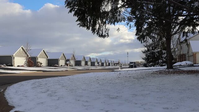 Fresh snow covering the grass on a long row of duplex homes down a subdivision street with branches from a pine tree in the foreground.