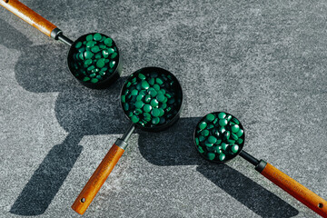 Algae superfood.Spirulina Tablets in Measuring Cups on Gray Surface. 