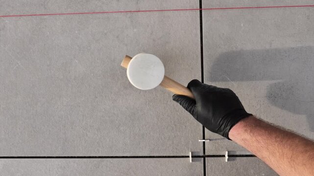 Laying tiles. Laying gray terrace tiles.A construction hammer taps tiles. Hands in black gloves lay tiles on a terrace. Terrace construction. 4k footage