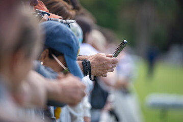 a man's hand writing a message on a cell phone in a line of people at a sports event in Argentina