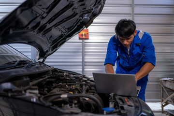 Mechanic analyzing car engine with laptop in garage
