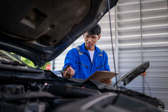 Asian mechanic inspecting car engine with checklist