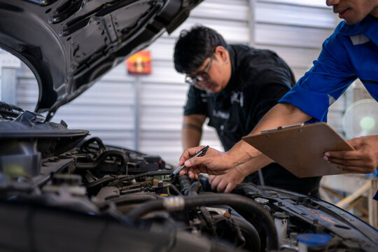 Mechanics inspecting car engine with checklist in garage