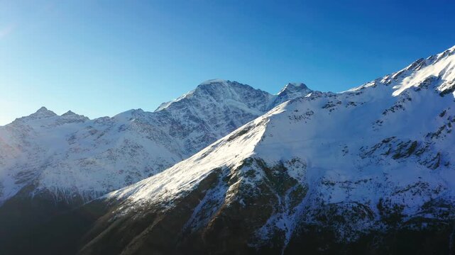 view of the snow covered peaks of the Caucasus Mountains in the North Caucasus region of Russia. The footage captures the rugged beauty of the alpine landscape with bright sunlight illuminating the sn